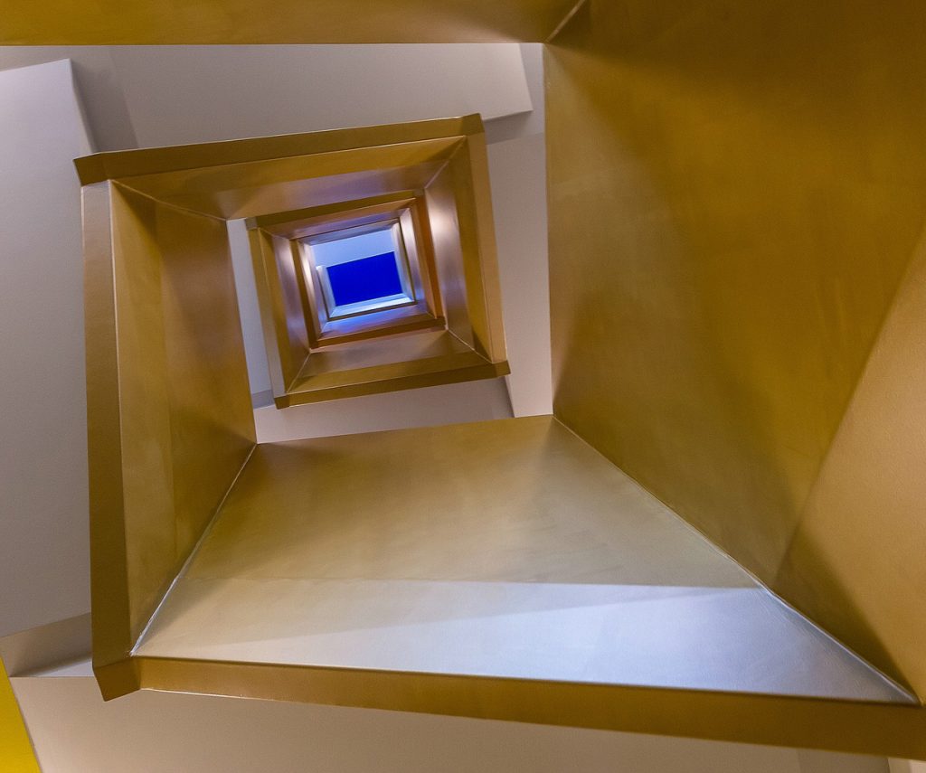 Blick nach oben durch ein quadratisches Treppenhaus mit gleichmäßiger Beleuchtung auf jeder Ebene.