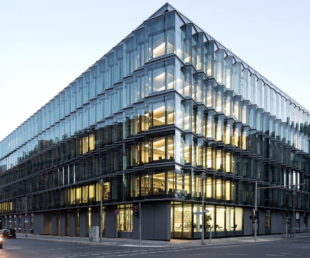 Ein modernes Bürogebäude mit Glasfassade, das von innen beleuchtet ist.