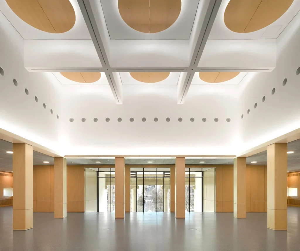 Heller Innenraum des Wilhelmpalais Stuttgart mit hohen Decken, runden Deckenaussparungen, symmetrischen Säulen und großem Eingangsbereich mit Glasfront