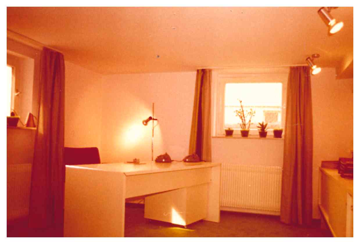 Ein schlicht eingerichteter Raum mit einem Tisch, beleuchtet durch warmes indirektes Licht an Wand und Decke. Das ist das erste Büro von Altena Licht in Weinstadt